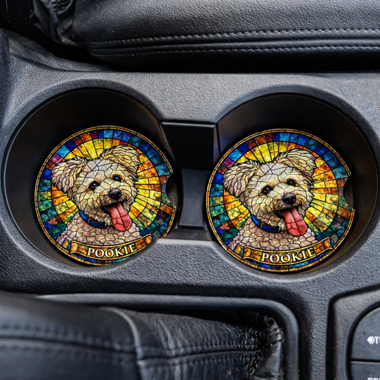 Two colorful dog coasters with 'Pookie' on a car's cup holder tray.