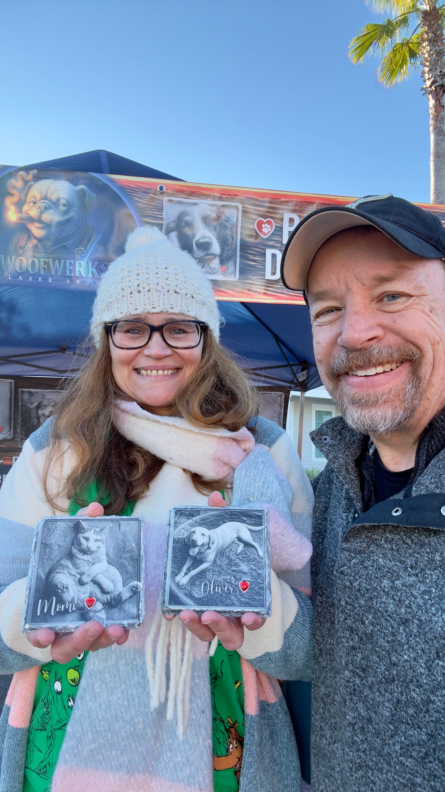 Two people holding small photo albums with a clear sky and palm tree in the background