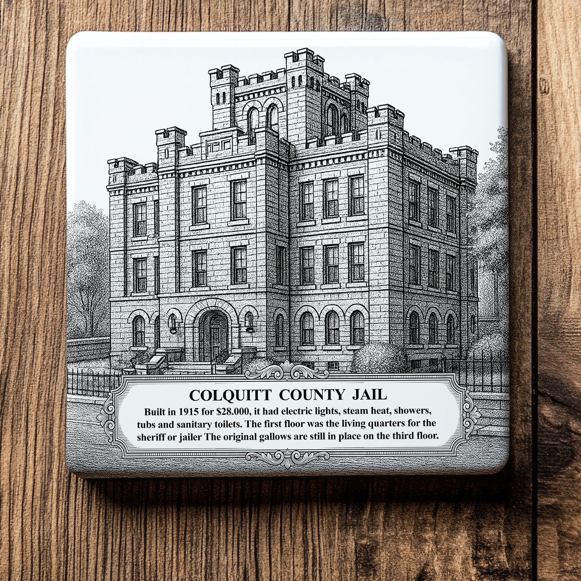 White ceramic coaster with a vintage pen-and-ink engraving of the castle-like historic Colquitt County Jail in Moultrie, Georgia. Features detailed stone texture, a historical fact banner at the bottom, displayed flat on a wood background.